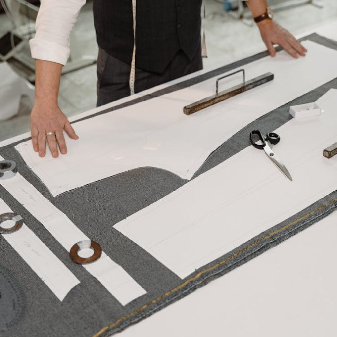 Proses membuat pola pakaian di atas kain menggunakan kertas pola, pembaris dan gunting di meja kerja jahitan